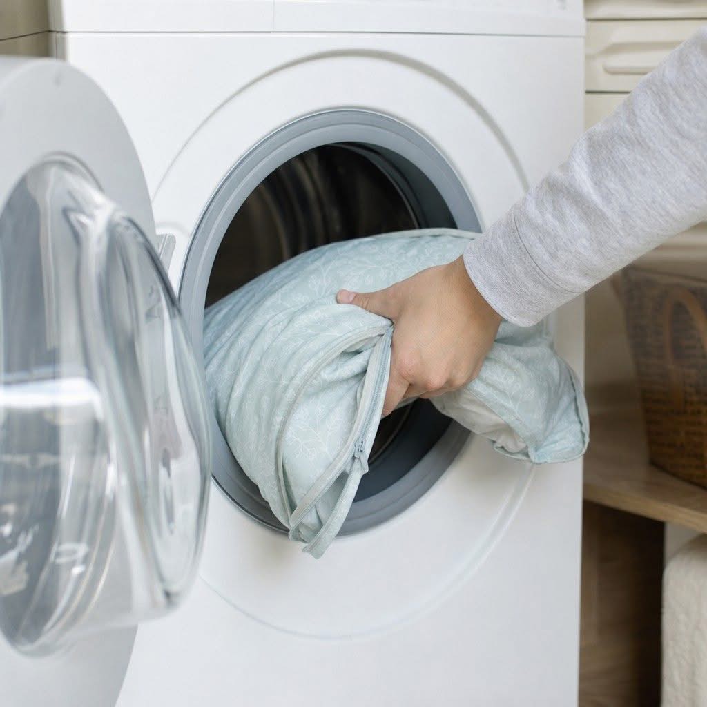 A removable nursing pillow cover being placed into a front-loading washing machine