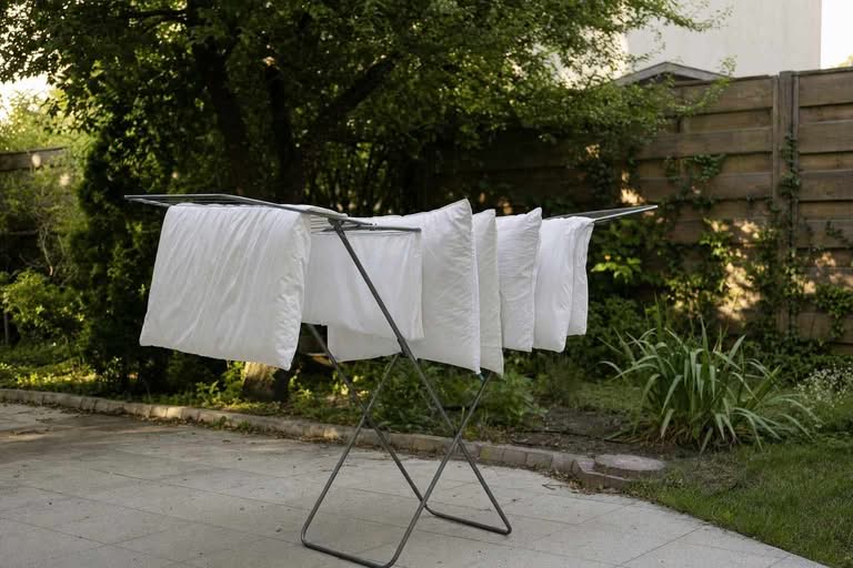Several white bed pillows hanging to air-dry on a clothes rack outdoors in soft daylight