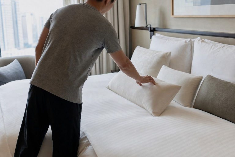 A hotel guest choosing one pillow from several arranged on a neatly made bed