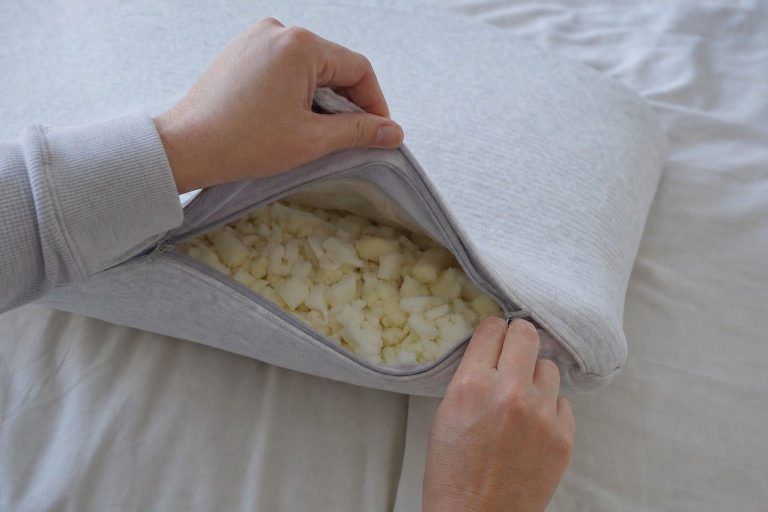 Hands opening the zip of an adjustable shredded memory foam pillow with loose fill visible
